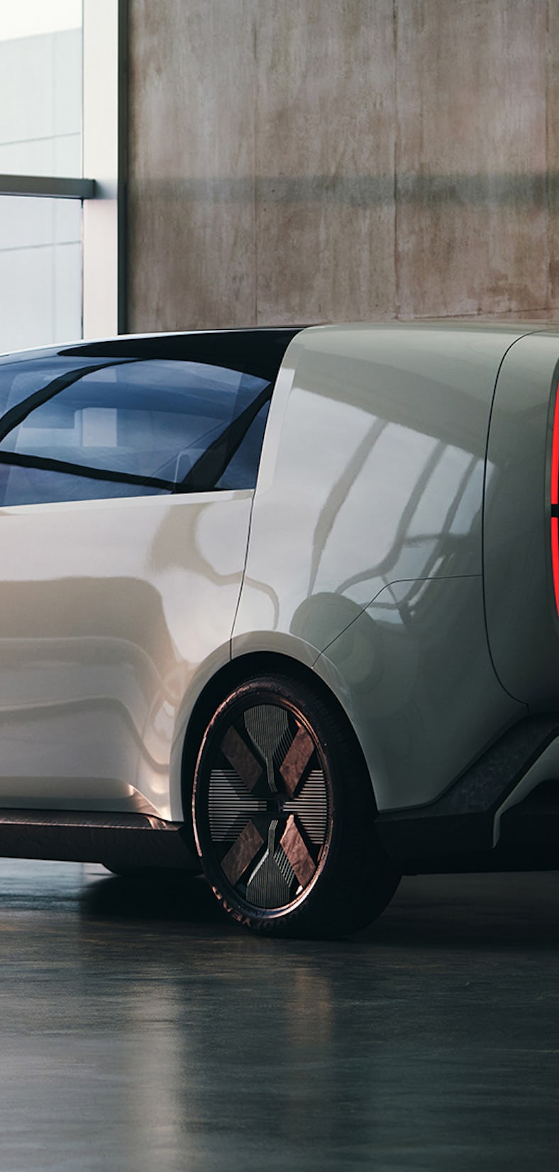 A futuristic electric vehicle with a boxy design and a red illuminated rear panel is parked in a mod...