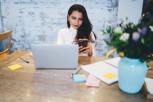 Young attractive woman in casual wear using phone discussing with colleague strategy of project spen...